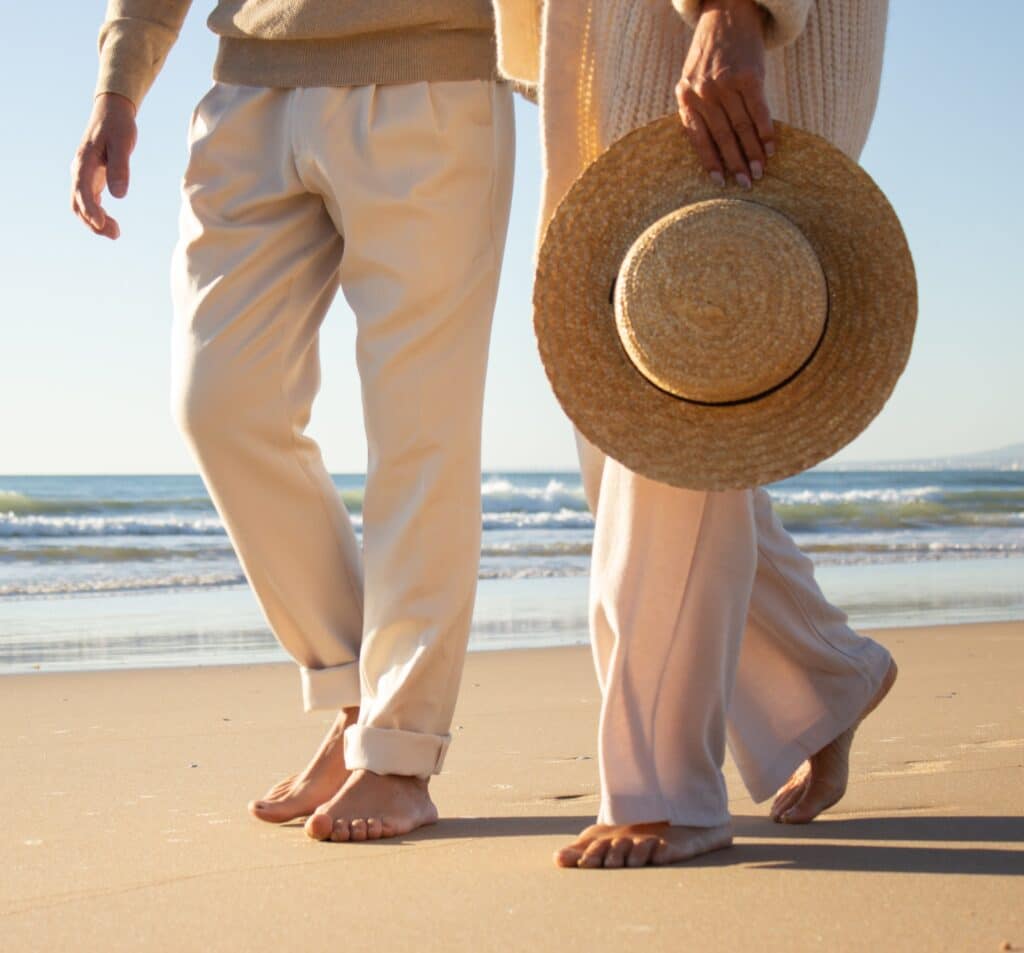 Marche romantique d'un couple pieds nus sur la plage Couple marchant pieds nus sur une plage ensoleillée, femme tenant un chapeau de paille.