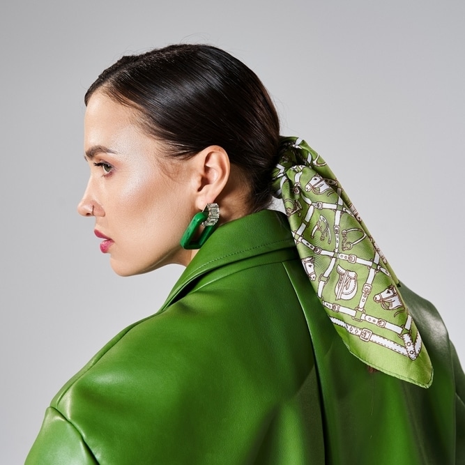 Look Monochrome Vert : Veste en Cuir et Foulard Soie Profil d'une femme en veste de cuir verte avec un foulard équestre noué dans les cheveux et boucles d'oreilles.