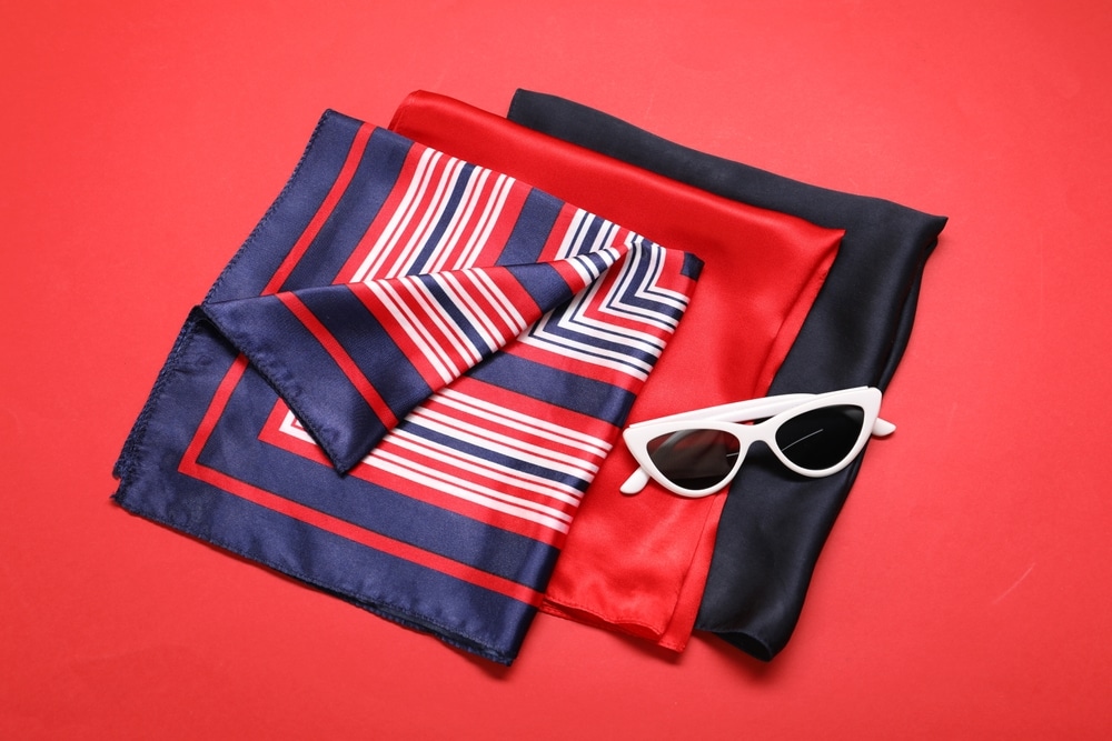 Accessoires mode chic : foulards soie et lunettes blanches Foulards en soie rayés, rouges et noirs avec des lunettes de soleil blanches œil de chat sur fond rouge.