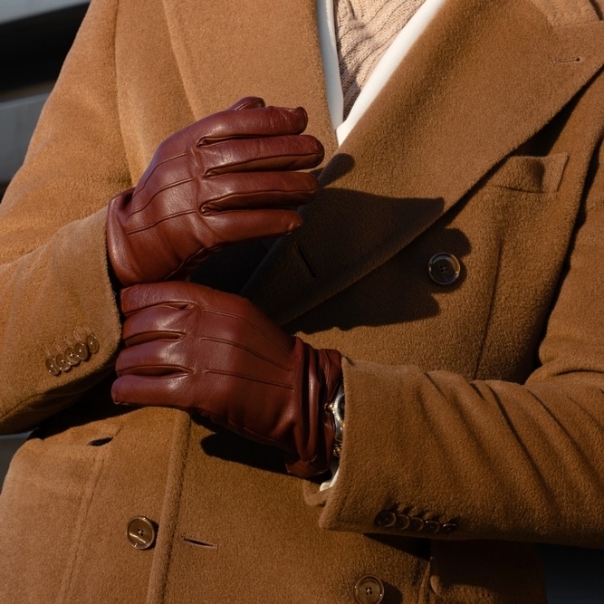 Look d'Hiver Homme : Gants en Cuir Marron et Manteau Camel Homme ajustant des gants en cuir marron portés avec un manteau camel élégant, style masculin raffiné.