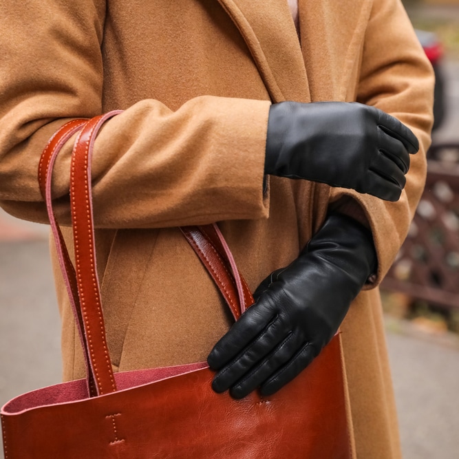 Gants en Cuir Noir et Manteau Camel : Style Hivernal Chic Femme portant un manteau en laine camel, des gants en cuir noir et un sac cabas rouge brique élégant.